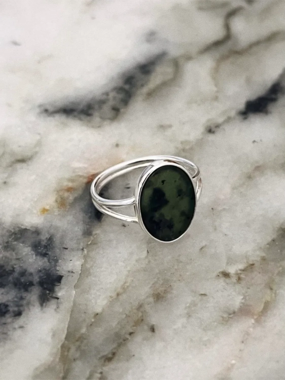 Pierścionek srebrny z owalnym nefrytem o głębokiej zieleni zaprezentowany na jasnym kamieniu.