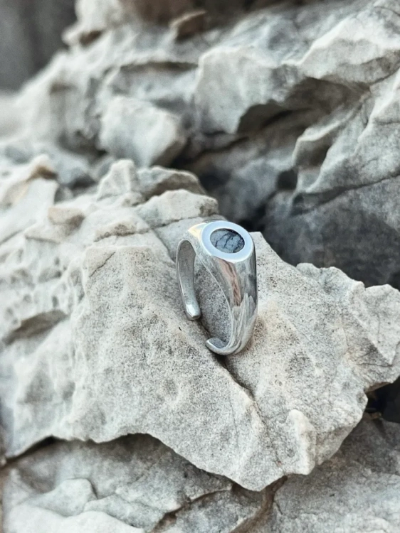 Srebrny sygnet z dolomitem Picasso na tle naturalnych skał.