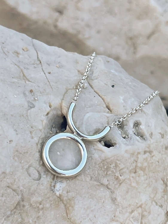 Naszyjnik z kryształem górskim sfotografowany na jasnej skale.