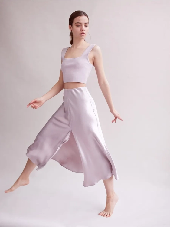 Modelka w zwiewnej sukience prezentuje minimalistyczną złoconą bransoletkę na kostkę na bosej stopie.